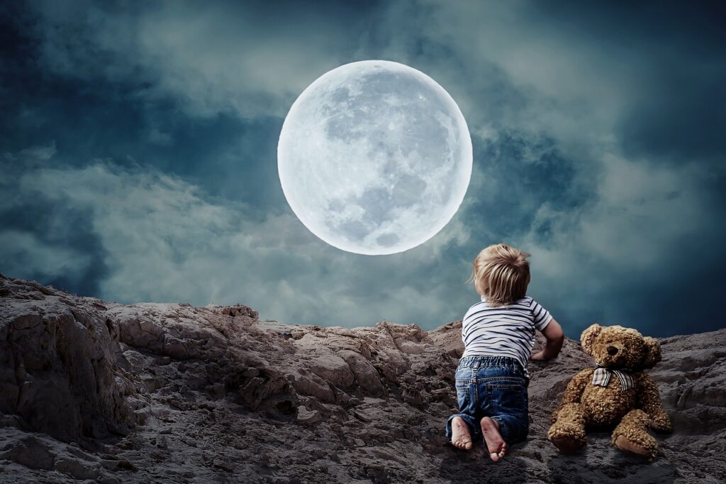 A young child gazing at a bright full moon in a rocky outdoor setting, accompanied by a teddy bear, under a cloudy night sky.